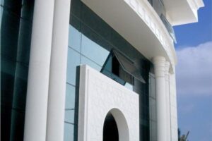 Nowoczesny budynek z białą fasadą, szklanymi okna i kolumnami.