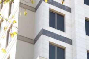 Nowoczesny budynek z białą fasadą, ciemnymi oknamiprzyziemisz i rośliną po lewej - Metamar