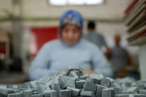 Pracownik w niebieskiej czapce przy stercie szarych metalowych elementów - Metamar