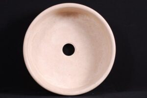 Okrągła kremowa umywalka z otworem odpływowym na czarnym tle.