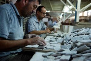 Dwaj mężczyźni pracują przy stole z kamiiennymi elementami w hali przemysłowej - Metamar