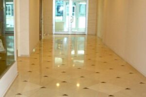 Pusty korytarz z beżową posadzką, szklanymi drzwiami i oknami.