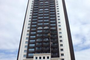 Wysoki blok mieszkalny z białymi i czarnymi fasadami, liczne okna, pochmurne niebo. - Metamar