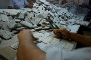 Ręce pracownika sortujące zabytkowe kafle cementowe na stole roboczym.