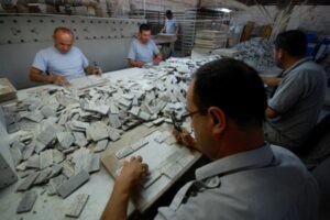 Pracownicy przy stołach sortują tysiące małych kartonowych kawałków w fabryce.