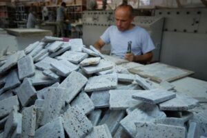 Mężczyzna w niebieskiej koszulce przy stosie szarych płytek kamiennych w warsztacie - Metamar