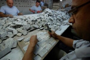 Pracownicy sortują białe kawałki materiału na stole warsztatowym.