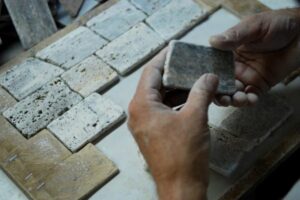Dłoń trzymająca kamienną płytkę obok ułożonych próbek materiału