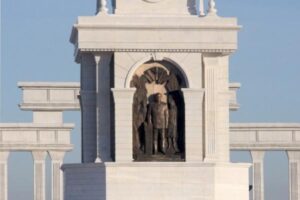 Biały pomnik z posągiem anioła w niszą i kolumnami.