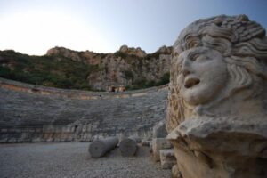 Kamienna głowa rzeźby przy ruinach antycznego amfiteatru w górach.