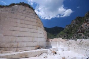 Kamieniołom z białym marmurem, masywną ścianą skalną i zieloną górą pod błękitnym niebem.