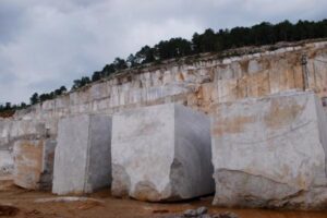 Kamieniołom marmuru z białymi blokami kamienia i lasem na szczycie wzgórza.