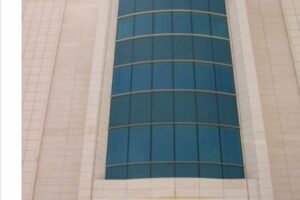 Nowoczesny budynek z zaokrągloną fasadą, niebieskie okna, beżowe płytki - Metamar