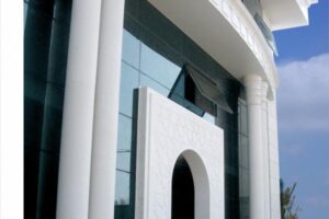 Nowoczesny budynek z białą fasadą, szklanymi okna, kolumnami i łukowatym wejściem - Metamar