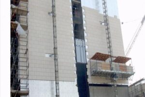 Budowa wielopiętrowego budynku z rusztowaniem i windą budowlaną.