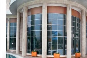 Nowoczesny budynek z zaokrąglonymi kolumnami, dużymi oknami i pomarańczowymi doniczkami.