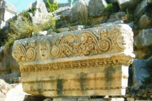 Ozdobna kamienna kolumna z rzeźbionymi głowami i ornamentami. - Metamar