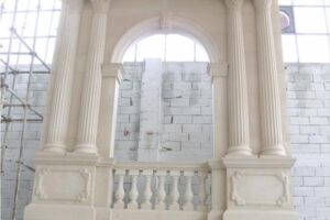 Białe kolumny i balustrada przy łukowym oknie, widok na ceglany mur.