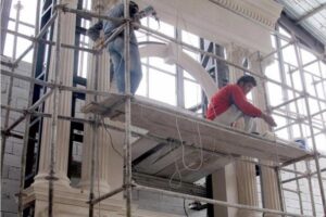 Pracownicy na rusztowaniu podczas prac remontowych w budynku.