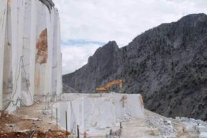 Koparka na terenie górniczym ze skałistymi góry w tle - Metamar