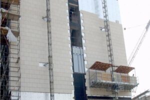 Budowa wielopiętrowego budynku mieszkalnego z fasadą z białych płyt, metalowymi podjazdami i rusztowaniem.