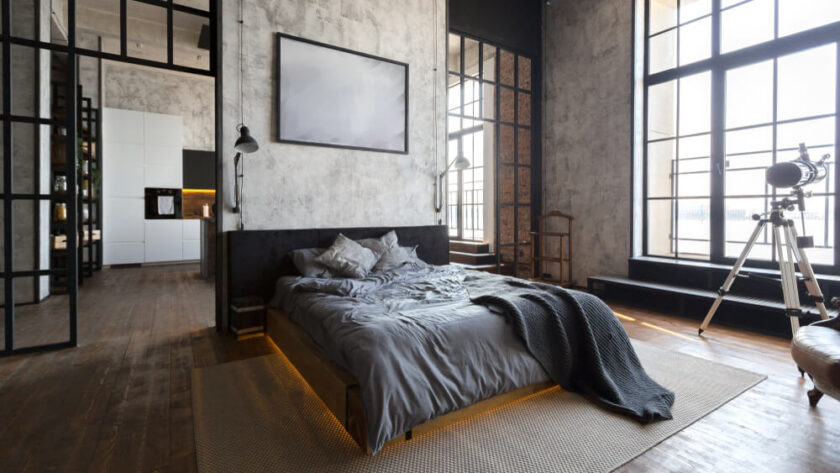 Nowoczesna sypialnia loft z łóżkiem, betonowymi ścianami i dużymi oknami.